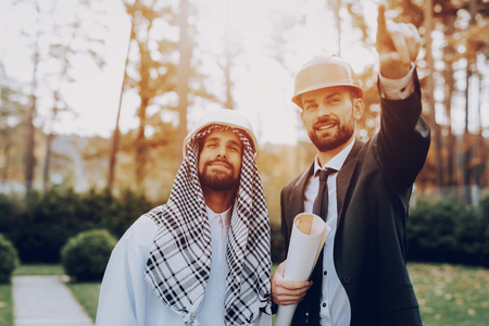 Girl Shows Construction Plan To Arab Businessman. Money Investment. Partnership Agreement. Graffic Design. Working With A Manager. Disdash And Keffiyeh Wearing. Business Discussion.の写真素材