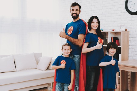 Young Family In Superhero Suits. Posing Concept. T-Shirts And A Raincoats. Bright Room. Resting Together. Save The World. Get Ready. Arms Akimbo. Kids With A Parents. Active Lifestyle.の写真素材