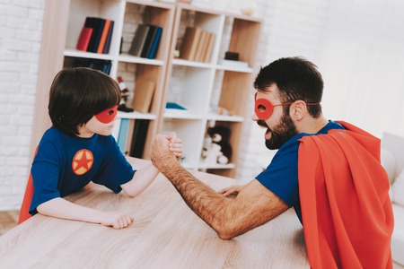 Father And Son. Red And Blue Superhero Suits. Arm Wresling Competition. Masks And Raincoats. Bright...