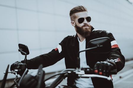Man In Leather Jacket Is Sitting On Motorcycle. Going For Ride. Fashion Rider. Confident Stare. Speed Vehicle. Cool Biker With A Beard. Motorbike Concept. Classic Style. Ready To Drive.の写真素材