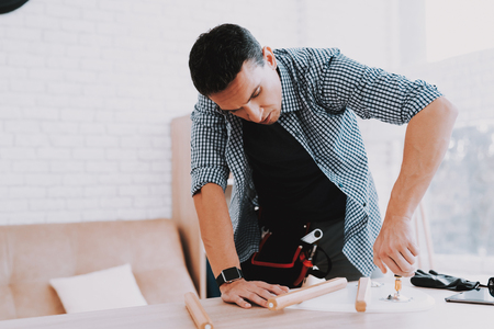 Young Man Assembling Coffee Table and Stools. Furniture Fittings. Engineer with Tool. Young Man at Home. Wooden Coffee Table. Selfmade Furniture. Man and Hobby. White Table in Room.の写真素材