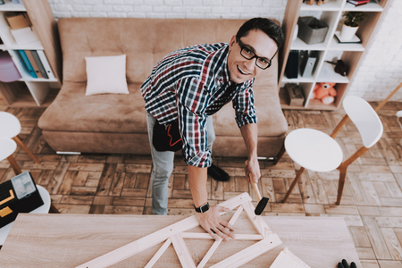 Young Man Assembling Wooden Bookshelf at Home. Wooden Bookcase. Selfmade Furniture. Man and Hobby. White Room. Engineer with Tool. Young Man at Home. Homemade Decoration. Modern Furniture.の写真素材