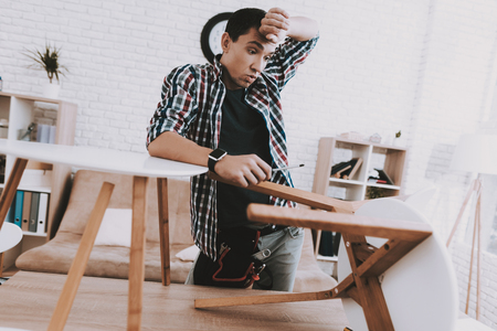 Young Man Assembling Coffee Table and Stools. Furniture Fittings. Engineer with Tool. Young Man at Home. Wooden Coffee Table. Selfmade Furniture. Man and Hobby. White Table in Room.の写真素材