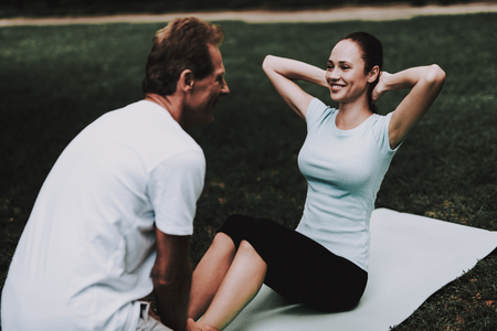 Young Couple in Sportswear Doing Yoga in Park. Sport and Healthcare Concept. Young Man Outdoor. Summer Park. Fun Outdoor. Sport in Summer. Trainer in Summer Park. Smiling Young Woman.の写真素材