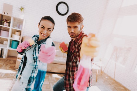 Young Couple in Checkered Shirts Cleaning Room. Sanitary at Home. Hands in Rubber Gloves. Housekeeping Concept. Cleaning with Sponge. Using Spray. Family at Home. Couple Indoor. Sanitary Concept.の写真素材