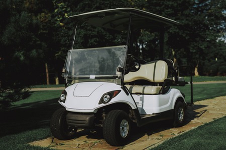 White Little Cart on Golf Field in Sunny Day. Healthy Lifestyle Concept. Golf Club. Sports in Summer. Vehicle on Field. Family Holiday. Outdoor Fun in Summer. Sunny Day. Electric Car.の写真素材