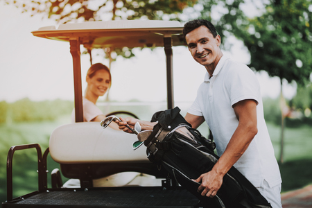 Happy Young Couple in White Cart on Golf Field. Young Family. Golf Club. Sports in Summer. Vehicle on Field. Outdoor Fun in Summer. Driver with Car. Healthy Lifestyle Concept. Couple on Vacation.の写真素材