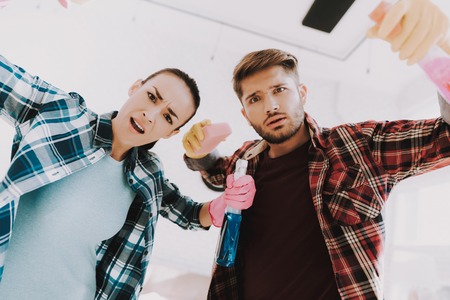 Young Couple in Checkered Shirts Cleaning Room. Sanitary at Home. Hands in Rubber Gloves. Housekeeping Concept. Cleaning with Sponge. Using Spray. Family at Home. Couple Indoor. Sanitary Concept.の写真素材