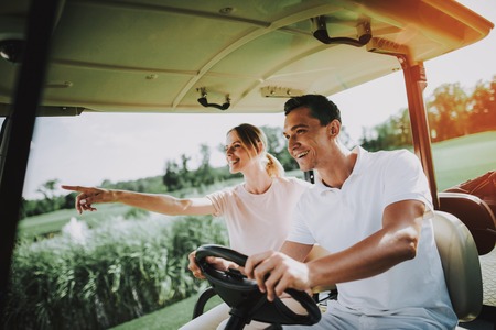 Happy Young Couple in White Cart on Golf Field. Young Family. Golf Club. Sports in Summer. Vehicle on Field. Outdoor Fun in Summer. Driver with Car. Healthy Lifestyle Concept. Couple on Vacation.の写真素材