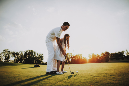 Father Playing Golf with Little Daughter on Field.. Relaxing in Golf Club. Sports in Summer. Outdoor Fun in Summer. Family Fun. Healthy Lifestyle Concept. Little Girl. Green Grass.の写真素材