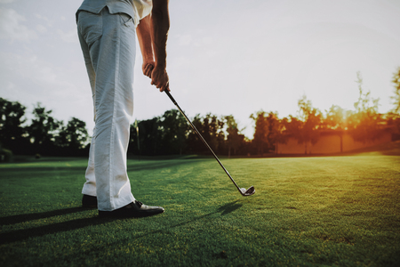 Young Man in White Clothes Playing Golf on Field. Relaxing in Golf Club. Sports in Summer. Outdoor Fun in Summer. Happy Young Man. Healthy Lifestyle Concept. Man it White Shirt. Green Grass.の写真素材