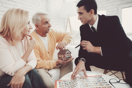 Man and Woman Consulting with Realtor in Office. Important Documents. Real Estate Conceps. Grandfather and Grandmother. People with Gray Hair. Young Realtor in Suit. House for Rent.の写真素材