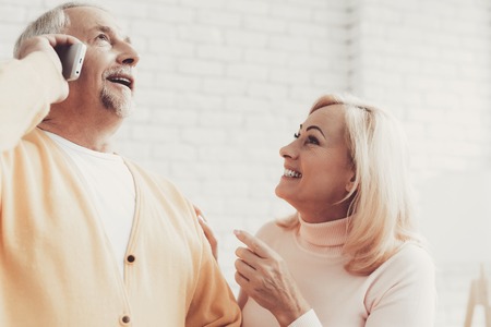 Smiling Old Man and Woman Talking on Smartphone. Sitting on White Sofa. Smiling Woman. Grandfather...