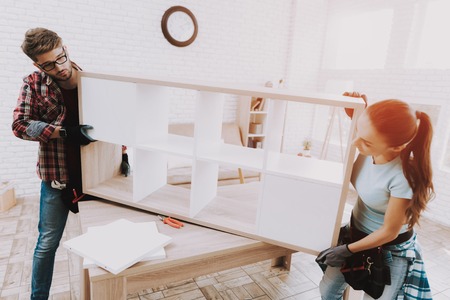 Young Couple Assembling Wooden Bookshelf at Home. Wooden Bookcase. Selfmade Furniture. Family at...