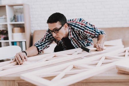 Young Man Assembling Wooden Bookshelf at Home. Wooden Bookcase. Selfmade Furniture. Man and Hobby. White Room. Engineer with Tool. Young Man at Home. Homemade Decoration. Modern Furniture.の写真素材