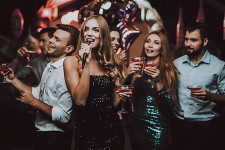 Woman in Black. Dress. Trendy Nightclub. Have Fun. Background. Cheerful. Smile. Smiling Girl.Singing Songs. Handsome Men. Beautiful Girls. Friends at Karaoke Club. Karaoke Club. Celebration.の写真素材