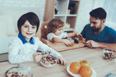 Smiling Kids.Happy Together. Leisure Time. Flakes with Milk. Father of Two Boys. Having Breakfast. Father. Man. Spends time. Sons. Engaged. Raising Child. Boy. Delicious Food. Child on Chair.Oranges.の写真素材