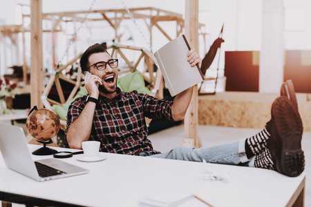 Folder. Talke on Phone. Feet on Table. Comfortable. Globe. Project. Laptop. Sit. Brainstorm. Young Guy. Businessman. Work. Office. Creative Worker. Ideas. Businesspeople. Workplace. Inspiration.の写真素材