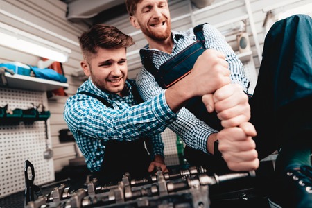 Two Auto Mechanics Work Together In Garage. Wrench Using. With All Might. Information Sharing. Professional Uniform. Confident Engineering Specialist Team. Service Station Concept.の写真素材