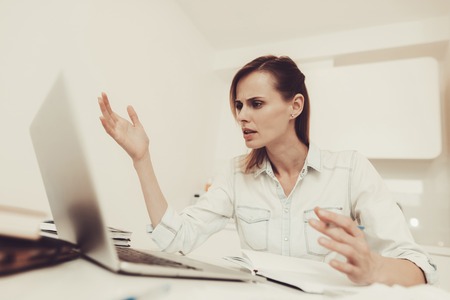 Young Woman Works With A Laptop At The Kitchen. Work From Home With A Notes Making Concept. Official Clothes. Bright Room. Comfortable Environment. Calmness And Confidence. Concentrated Worker.の写真素材