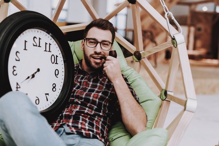 Big Watch. Hanging Chair. Clock. Eyeglasses. Young Male. Businessman. Working in Office. Creates Ideas. Eyeglasses. Workplace. Project. Sit. Brainstorm. Work. Office. Creative Worker. Inspiration.の写真素材
