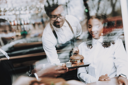 Barman. Burger. Black Man. Date. Girl. Cafe. In Love. Smile. Mulatto. Rest. Window. Have Fun. Food in Plate. Food to Customers'. Joyful. Leisure Time. Nightlife. Positive. Emotion. Clubbing.の写真素材