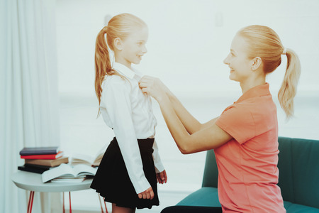 Young Mother Is Prepairing A Daughter For School. Studying Uniform. Black And White Clothes. Button Up. Proud Mum. Clean Dress. Ready To Learn. Family Relationship. Happy Smiling Kid.の写真素材