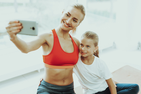 Mum And Daughter Are Doing Selfie On A Gym Carpet. Lotus Position. Relaxing Together. Fitness At Home. Holiday Leisure. Body Balance. Photo Posing. Family Relationship. Hug Each Other.の写真素材