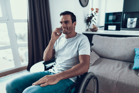 Disabled Person in Wheelchair Talking Phone. Handsome Smiling Person Sits Indoors in Bright Modern...