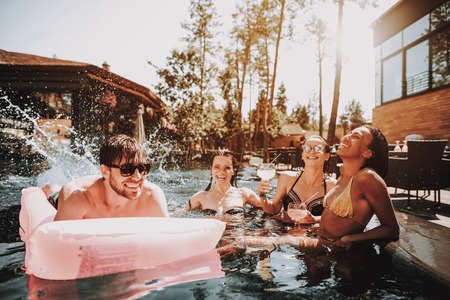 Group of Young Happy People Swimming in Pool. Young Smiling Friends wearing Sunglasses Laughing and Relaxing Together in Outdoor Hotel Pool next to Poolside. Summer Vacation Concept. Pool Partyの写真素材