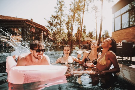 Group of Young Happy People Swimming in Pool. Young Smiling Friends wearing Sunglasses Laughing and Relaxing Together in Outdoor Hotel Pool next to Poolside. Summer Vacation Concept. Pool Party