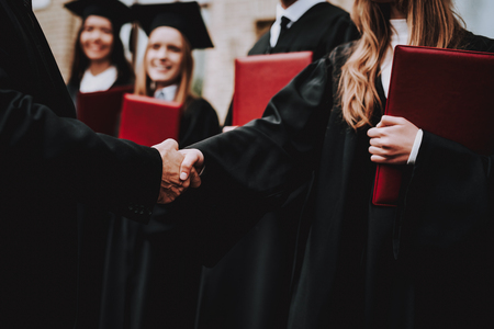 Handshake. Teacher. Students Diplomas. Courtyard. University. Finish Studies. Graduate. Guys. Greet. Group of Young People. Good Mood. Have Fun. Friendship. Knowledge. Cap. Cheerful. Celebration.の写真素材