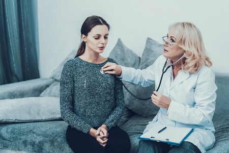 Young Slim Woman in Gray Sweater Visiting Doctor. Woman in White Coat. Diet and Healthcare Concept. Docror with Stethoscope. Women on Gray Sofa. Medical Equipment. Woman in Glasses.の写真素材