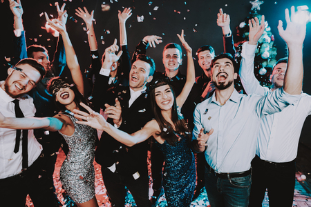 Smiling People Celebrating New Year on Party. Happy New Year. People Have Fun. Indoor Party. Celebrating of New Year. Young Woman in Dress. Young Man in Suit. Excited People. Hands Up.の写真素材
