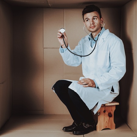 Doctor in Coat with Stethoscope in Cardboard Box. Young Man in White Coat. Life in Little Cardboard...