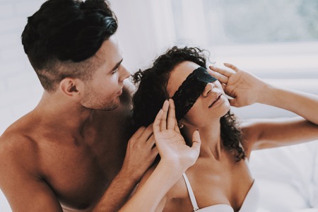 Passionate Attractive Couple in Underwear on Bed. Handsome Man Ties Woman's Eyes with Black Ribbon...