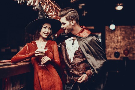 Young Man and Woman in Costumes at Halloween Party. Handsome Man and Beautiful Woman Wearing Halloween Costumes Standing next to Bar counter in Nightclub. Celebration of Halloweenの写真素材