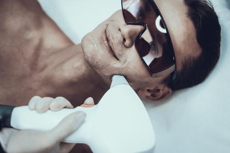 Young Man in Spa Salon for Laser Hair Removal. Guy in Beauty Salon. Modern Cosmetology. Proffesional Cosmetologist. Doctor with Laser Epilator. Men's Beauty Concept. Medical Equipment.の写真素材