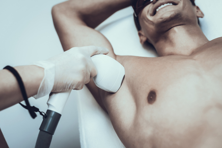 Young Man in Spa Salon for Laser Hair Removal. Guy in Beauty Salon. Modern Cosmetology. Proffesional Cosmetologist. Doctor with Laser Epilator. Men's Beauty Concept. Man in Glasses.の写真素材