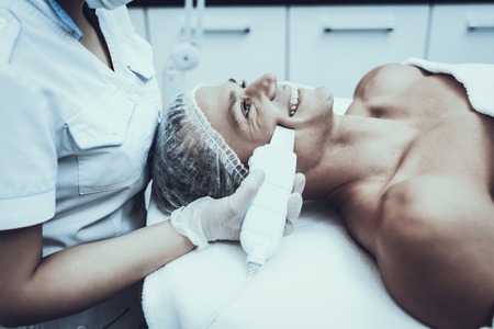 Young Man in Spa Salon for Laser Hair Removal. Guy in Beauty Salon. Modern Cosmetology. Proffesional Cosmetologist. Doctor with Laser Epilator. Men's Beauty Concept. Medical Equipment.の写真素材