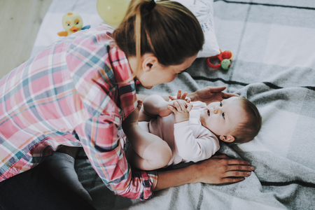 Young Mother Plays with Cute Baby Lying on Carpet.の写真素材
