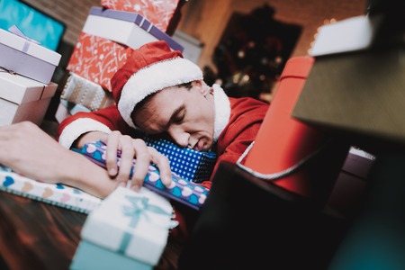 Young Man in Santa Claus Costume with Gift Boxes. New Year Eve. Christmas Tree in Office....