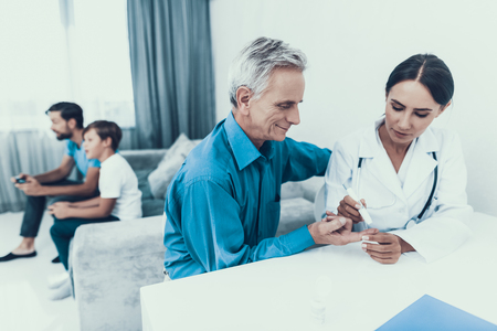 Doctor Visiting Family and Taking Blood Sample. Diabetes Concept. Sugar in Blood. Healthcare Concept. Young Woman in Uniform. White Coat. Medical Equipment. Glucometer in Hand. Medical Mask.の写真素材
