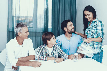Smiling Mother Pouring Water in Glasses at Home. Father and Son. Smiling People. Parenthood Concept. Family at Home. Happy Family. Glass of Water. Young Woman. Family in Dining Room.の写真素材