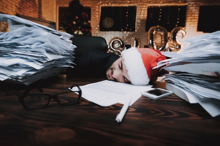 Tired Man Working with Documents on New Year Eve. Christmas Tree in Office. Business Concept. Man in...