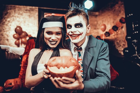 Portrait of Young Couple in Halloween Costumes. Beautiful Woman and Handsome Young Man Wearing Costumes holding Pumpkin at Halloween Party in Nightclub. Happy Friends having Fun Celebrating Halloweenの写真素材
