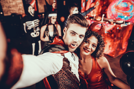 Young Couple in Halloween Costumes taking Selfie. Beautiful Woman and Handsome Young Man Wearing Costumes having Fun at Halloween Party in Nightclub. Happy Friends having Fun Celebrating Halloweenの写真素材
