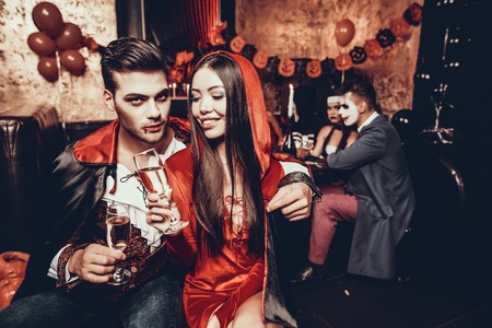 Young Couple Wearing Costumes Drinking Champagne. Group of Young Happy People in Costumes at Halloween Party Drinking Champagne and having Fun in Nightclub. Celebration of Halloweenの写真素材