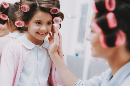 Little Lady with Curlers. Happy Child in Beauty Salon. Consept Beauty Salon. Beautiful Little Lady. Girl and Woman. Beautiful Face. Woman Admires Happy Child. Woman with Curlers. Smiling Person.の写真素材