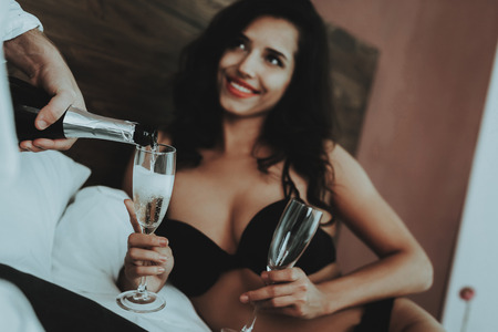 Brunette Girl. Person with Glasses Champagne. Mans Shirt. Man Pouring Glass Champagne. Woman with Sexy Man. White Shirt. Girl in Lingerie. Woman in Black Lingerie. Lying on Bed. He and She in Bedroom.の写真素材
